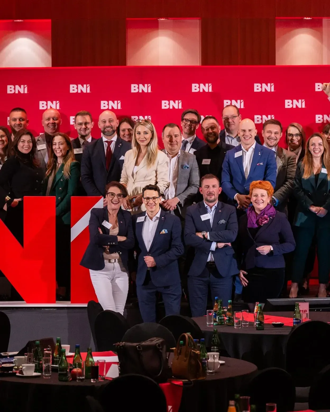 Kilkadziesiąt przedsiębiorczyń i przedsiębiorców pozuje razem przed ścianką z logotypami BNI.